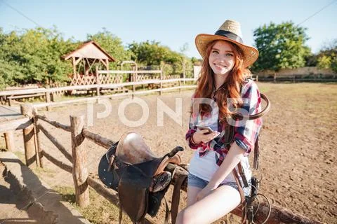 Smiling woman cowgirl standing and using mobile phone on ranch Stock Photos