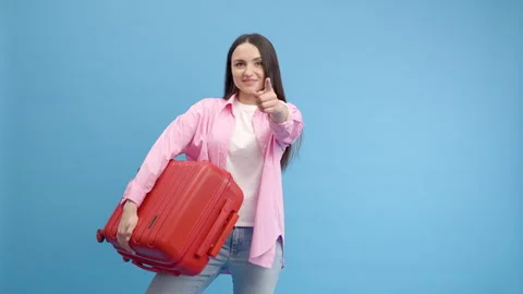 Smiling woman doing advertisement in studio on blue background with red suitcase Stock-Footage 250996461