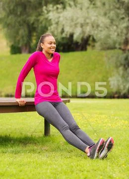 Smiling woman doing push-ups on bench outdoors Stock Photos