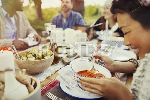 Smiling woman eating soup at patio table with friends Stock Photos