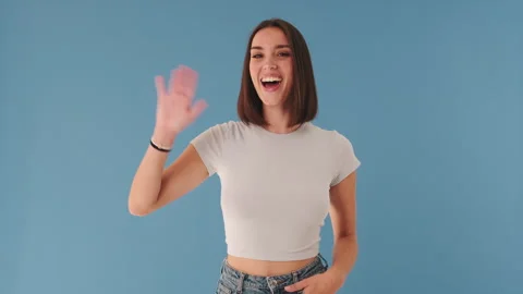 Smiling woman gesturing hello looking at camera isolated on blue background in Stock Footage 255504832