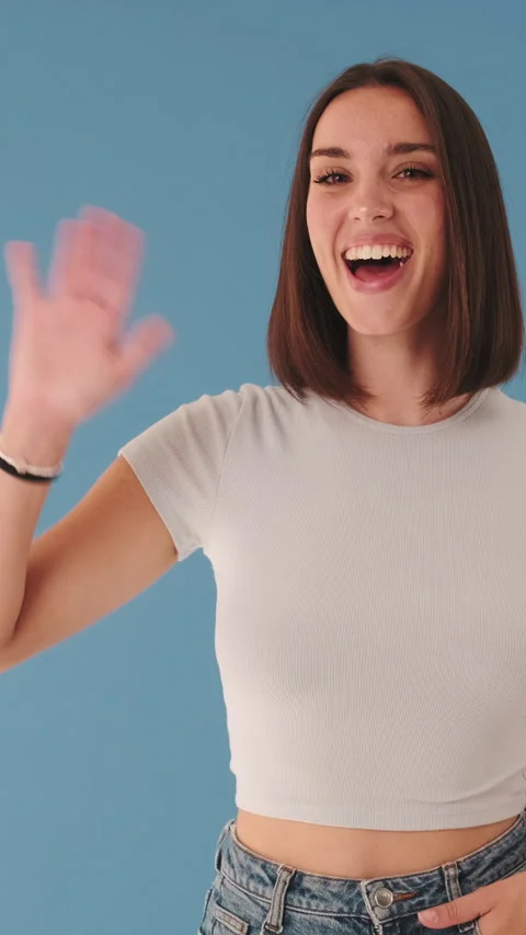 Smiling woman gesturing hello looking at camera isolated on blue background in Stock Footage 255504907