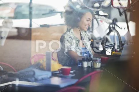 Smiling woman with headphones at laptop in cafe Stock Photos