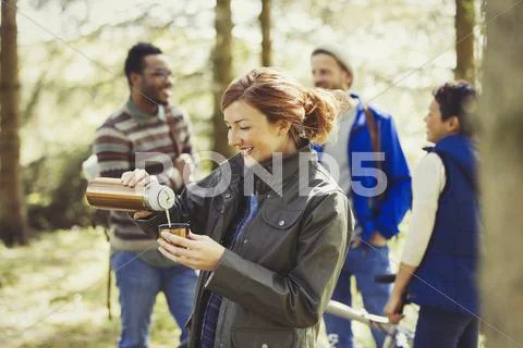 Smiling woman hiking pouring coffee from insulated drink container in woods Stock Photos