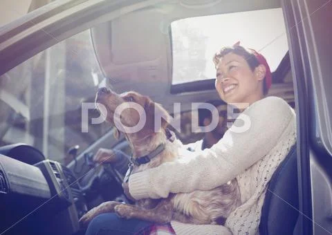 Smiling woman holding dog on lap in car Stock Photos