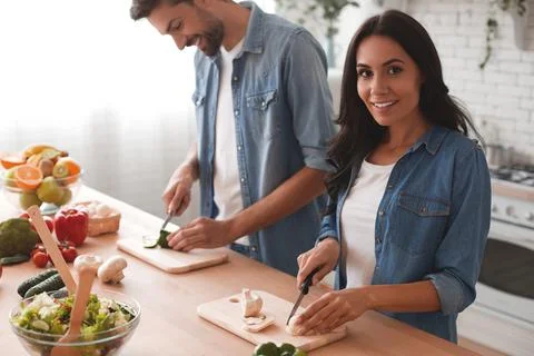 Smiling woman looking at the camera while slicing vegetables with man togethe Stock Photos