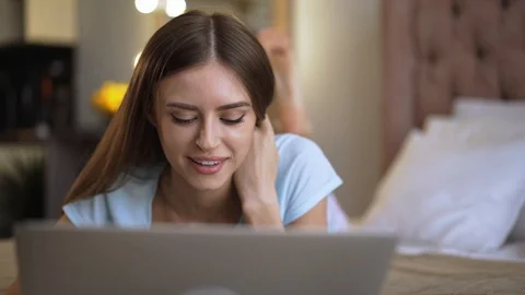 Smiling woman lying on her bed and web surfing on her laptop Stock Footage