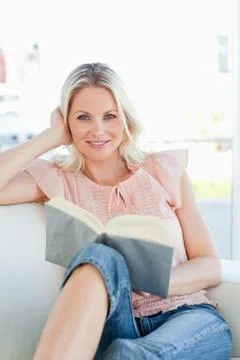 Smiling woman lying on a sofa while reading a book Photos