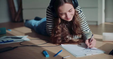 Smiling woman lying while drawing and listening to music Stock Footage 268219360