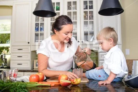 Smiling woman making smoothie for small boy Stock Photos