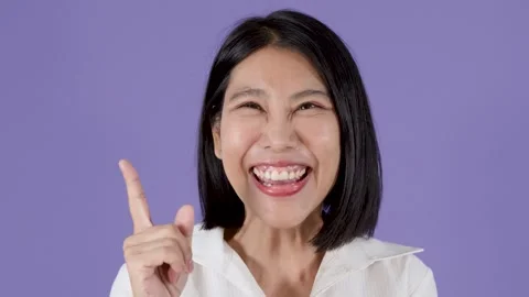 Smiling Woman Pointing Up Against Solid Purple Background Stock Footage 323496942