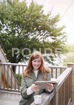 Smiling woman with red hair using digital tablet on cabin balcony Stock Photos