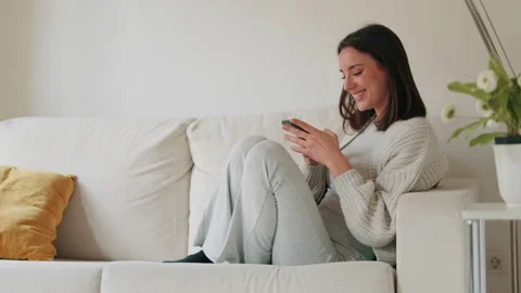 Smiling Woman Relaxing on Sofa Using Phone Stock Footage 316569875