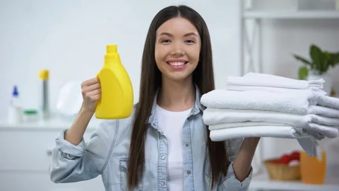 Smiling woman showing clean towels and laundry detergent, fabric softener Stock Footage