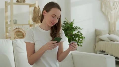 Smiling woman sitting on sofa using mobile phone, hold credit bank card Stock-Footage 150026073