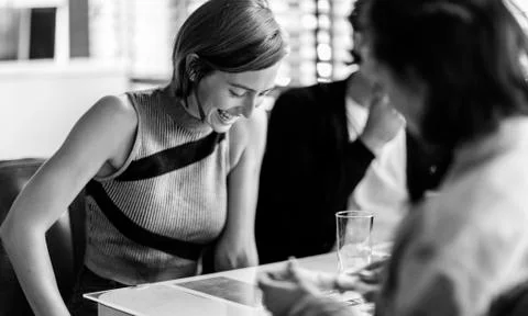Smiling woman sitting with two friends in a booth in a diner, looking down. Stock Photos