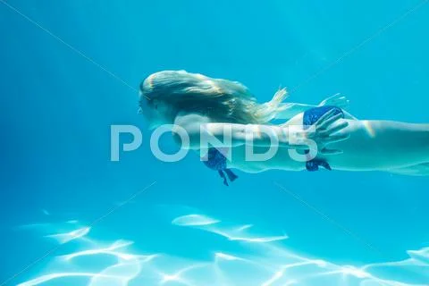 Smiling Woman Swimming Underwater In Swimming Pool