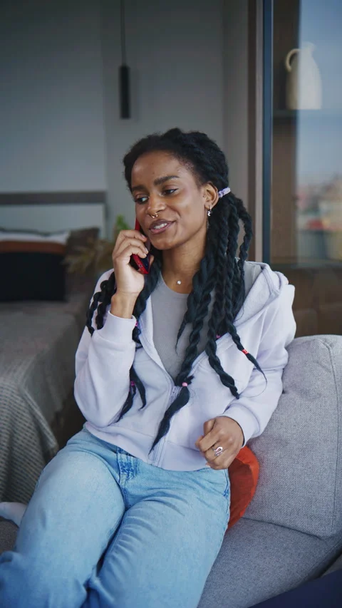 Smiling woman talking on the phone while sitting in a cozy room with a large win Stock Footage 339368037