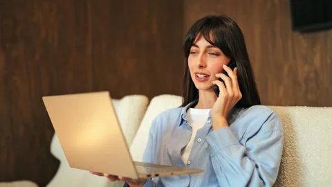Smiling Woman Talking on Smartphone While Working Remotely on Laptop 스톡 동영상 313946313