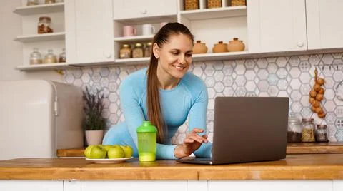 Smiling woman using computer in modern kitchen. Healthy lifestyle concept Stock Photos