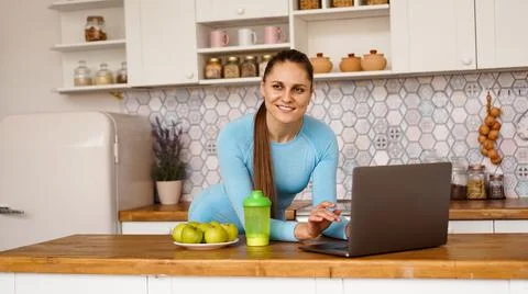 Smiling woman using computer in modern kitchen. Healthy lifestyle concept Stock Photos