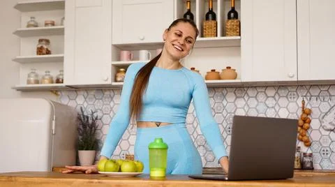 Smiling woman using computer in modern kitchen. Healthy lifestyle concept Stock Photos