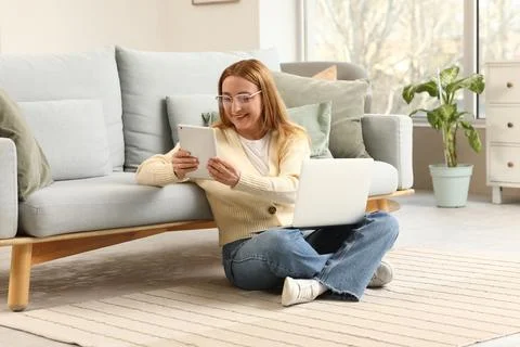 Smiling woman using digital tablet and laptop on floor, remote work and onlin Stock Photos