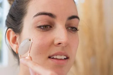 Smiling woman using face roller on her cheek while doing her beauty routine Foto stock