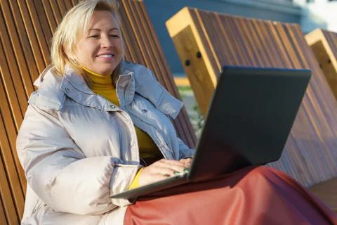 Smiling woman using laptop on a bench. Stock Photos