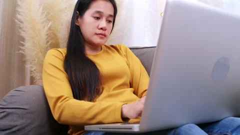 Smiling woman using laptop sitting on couch at home. Women sitting on sofa us Stock Footage 158934153