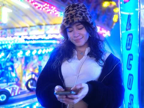 Smiling woman using the mobile next to a sign of a fairground attraction Stock Photos