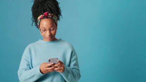 Smiling woman using mobile phone on blue background in studio Stock Footage 301456940