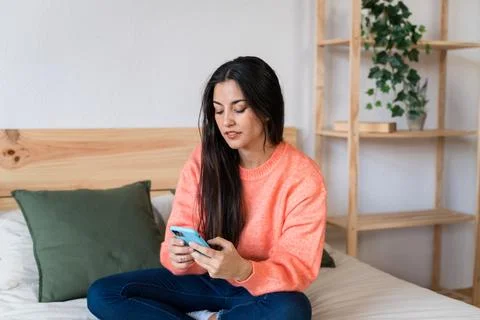 Smiling woman using smartphone on bed Stock Photos