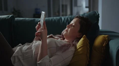 Smiling woman using smartphone while lying on living room sofa Stock Footage 234342488