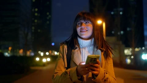 Smiling woman using smartphone while walking in the city at night Stock Footage 328911492