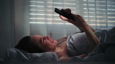 Smiling Woman Using Smartphone While Lying in Bed at Night Video stock 329670790
