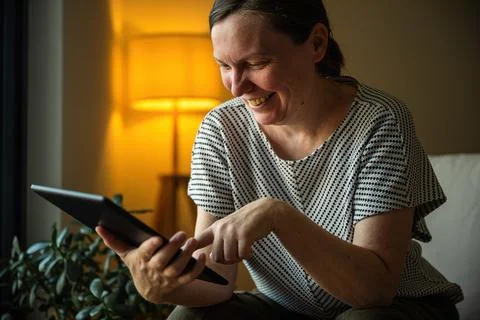 Smiling woman using a tablet computer in a comfortable home setting during .. Stock Photos