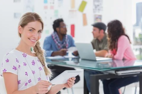 Smiling woman using tablet with creative team working behind Stock Photos