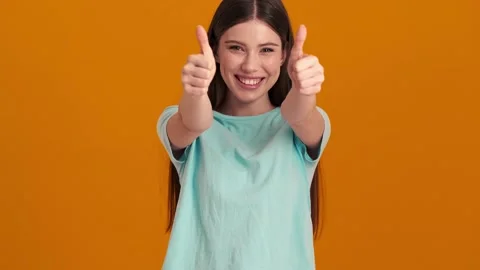 A smiling woman wearing basic T-shirt doing thumb-up gesture in orange studio Video stock 154316523