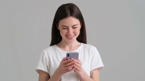 A smiling woman wearing basic T-shirt is using her smartphone  Stock Footage 154945978