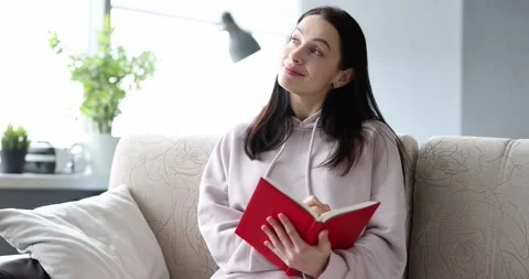 Smiling woman writing diary notes while sitting on sofa at home Stock Footage 284748347