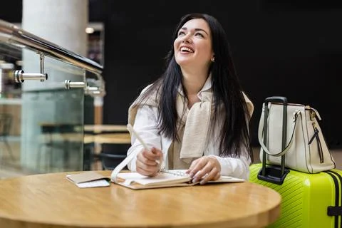 Smiling woman writing making notes in diary sitting at table in international Stock Photos