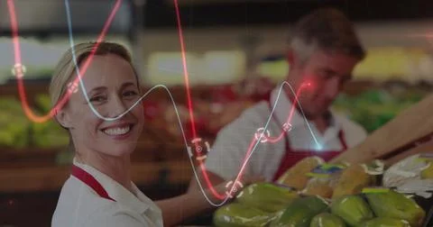 Smiling worker wearing red apron sorting produce in produce aisle with graphs Stock Photos
