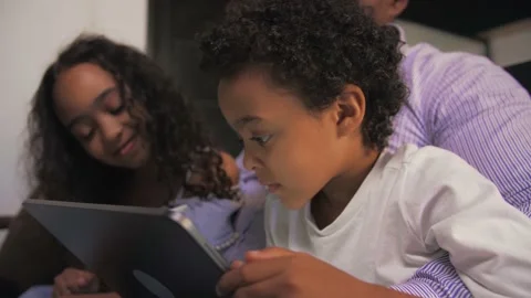 Smiling Young African boy draws on a tablet sitting on the couch with family Stock Footage 201292526