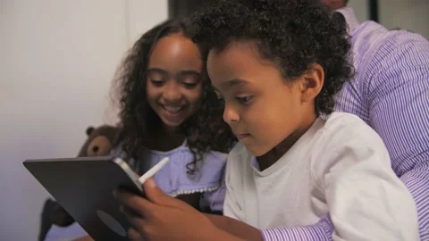 Smiling Young African boy draws on a tablet sitting on the couch with his family Stock Footage 201292539