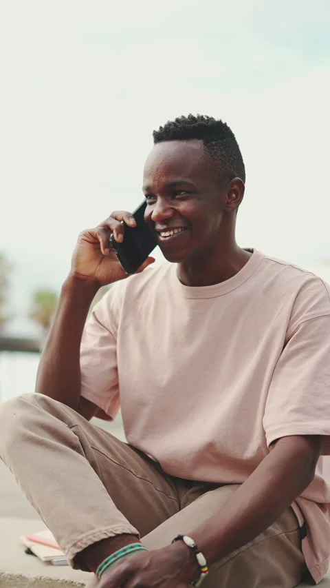 Smiling young african student sitting outside of university talking on cellphone Stock Footage 226936076