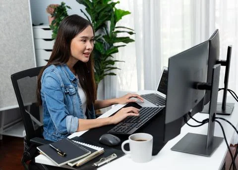 Smiling young Asian IT developer working software on two screens. Stratagem. Foto stock