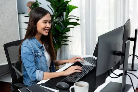 Smiling young Asian IT developer working software on two screens. Stratagem. Stock Photos