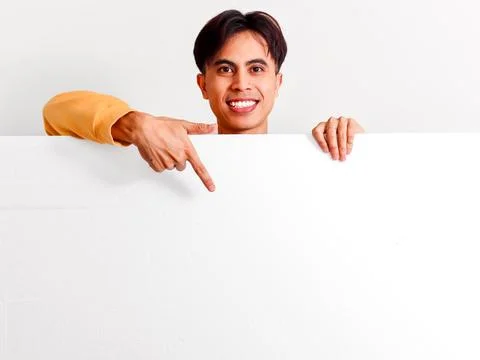 Smiling young Asian man looking over board and pointing finger down at copy.. Stock Photos
