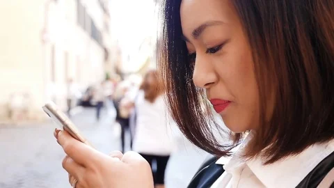 Smiling young asian woman's profile typing on the smartphone in the street Stock Footage 75200318